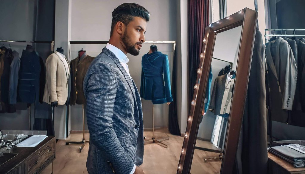 man stands in front of a full-length mirror inside a modern tailoring studio